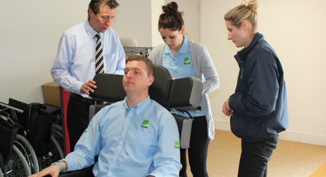 Healthcare Professional Demonstrates Chair to three others. 