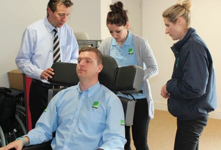 Healthcare Professional Demonstrates Chair to three others. 