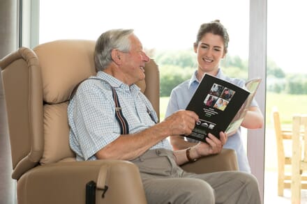 Elderly man in Specialist Seating Reading to Visitor.